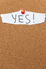 Handwritten note saying YES pinned to a cork board. This positive affirmation conveys agreement and encouragement, suitable for motivational content.