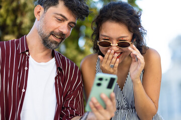 Smiling couple enjoying surprise on smartphone outdoors, sharing joyful moment under sunny skies