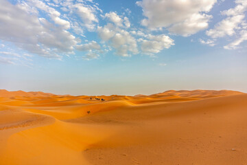 Golden sand dunes of Erg Chebbi desert in Morocco under blue sky with scattered clouds and distant...
