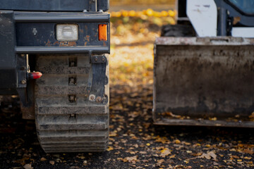 Tracked loader and metal bucket positioned on leaf-covered ground representing construction machinery reliability, strength, and precision engineering performance
