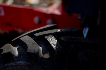 Wet tractor or loader tire with strong tread blocks illuminated by sunlight representing durability, strength, and off-road performance of industrial equipment