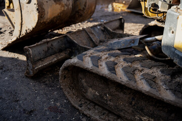 Detailed view of rubber track and steel blade of compact excavator showing terrain grip, mud adhesion and construction machinery ground contact on building site surface