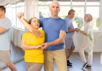 Obraz premium Happy smiling elderly man enjoying impassioned merengue with female partner in latin dance class. Social dancing concept..