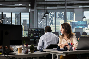 Business people using laptops and computers in bright workspace, analyzing projections, metrics and reports. Team focuses on business intel, insights and targets under executive management.