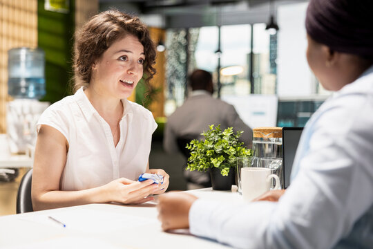 Businesswoman from HR offers access tag and identification badge to new hire, finalizing the onboarding and registration after resume and CV approval. Professional welcoming to the team.