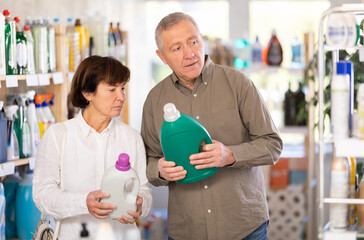 Couple elderly man and woman buyers choosing laundry detergent in household chemicals store