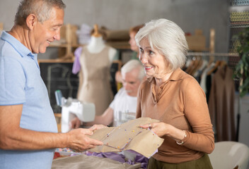 Obraz premium Elderly man and woman students discuss sewn pattern at sewing master class