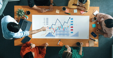 A diverse group of professionals collaboratively analyzing financial charts on a modern conference table, fostering teamwork and strategic planning in a dynamic office environment. Scalp