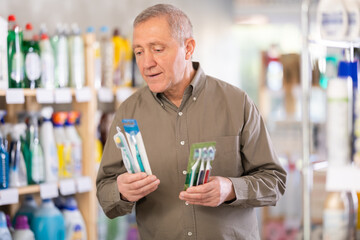 Elderly man holds several toothbrushes, carefully choosing them for his family. European buys dental hygiene products