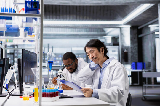 Senior laboratory scientist feeling neck ache while using computer to process DNA patient data for clinical research. Lab specialist pained by incorrect posture at PC, looking at genetic analysis - Powered by Adobe