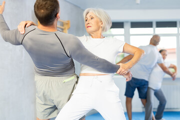 Aggressive old woman practicing self-defense techniques in pairs during workout session