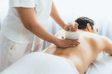 Hot herbal ball spa massage body treatment, masseur gently compresses herb bag on man body....