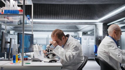 Male scientific expert observes specimen under microscope for bio science, experiment supports...
