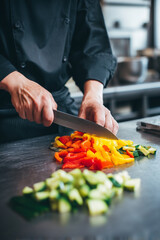 A chef chopping colorful bell peppers and zucchini for a vegan stir-fry at a stainless steel counter.