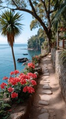 Scenic Coastal Pathway Lined with Vibrant Red Flowers and Lush Greenery Under a Clear Blue Sky with a Palm Tree Overlooking the Ocean