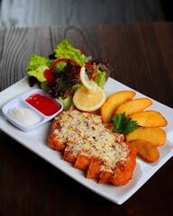 Chicken Schnitzel with Cheese, Potato Wedges, and Fresh Salad Served on White Plate