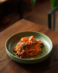Spaghetti Bolognese with Meat Sauce Served in Green Ceramic Bowl on Wooden Table
