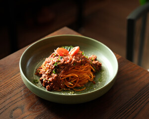Spaghetti Bolognese with Meat Sauce Served in Green Ceramic Bowl on Wooden Table