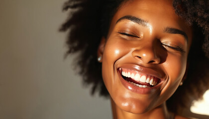 Smiling black woman with curly hair. Happy african american female model laughing. Closeup face of young woman with healthy skin, afro hairstyle. Woman with glowing skin, joyful expression on face.