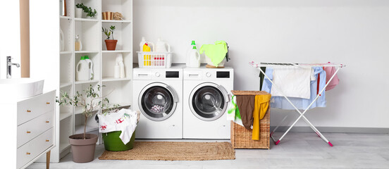Interior of light bathroom with washing machines, laundry basket and dryer