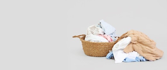 Wicker laundry basket and dirty clothes on light background with space for text