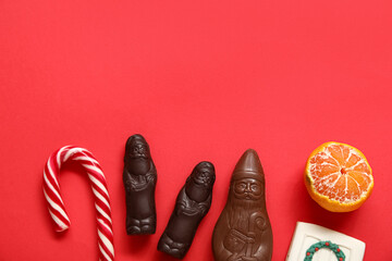 Chocolate Santa Clauses, candy cane and tangerine on red background