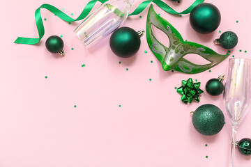 Composition with green carnival mask, champagne glasses and Christmas balls on pink background