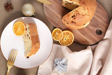 Plate with piece of Panettone, Christmas decor and dried orange slices on grey background