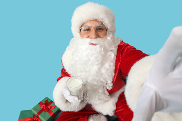 Santa Claus with glass of milk taking selfie on blue background, closeup
