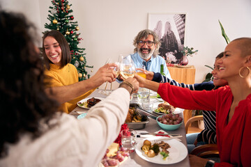 Diverse generations of happy Caucasian people celebrating domestic life toast with glasses white wine at home. Smiling family meeting enjoying Christmas meal together at festive holiday table indoors