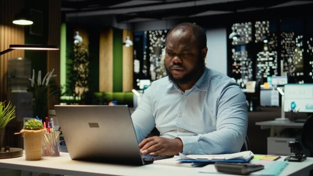 African american guy at the workspace sitting in deep concentration, pondering for a decision. Using laptop as he applies rational thinking and intuition for issue, mental haze. Camera A.