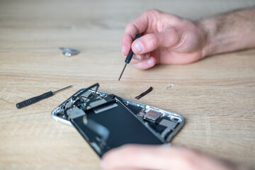 Smartphone repair process with screwdriver and disassembled mobile phone on wooden table. Tech service concept, technical support, service center, display replacement