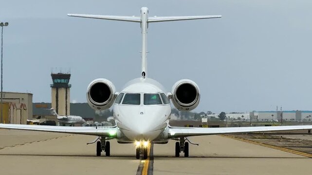 A large business jet taxiing is viewed head-on, on the taxiway centerline and strait at the camera.