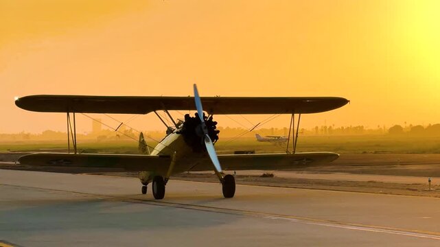 An antique yellow biplane swerves and sweeps on the taxiway, silhouetted and gleaming against the setting sun.