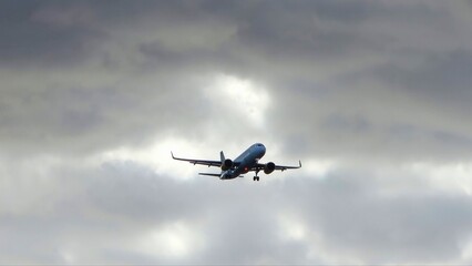 Commercial airplane flying with landing gear against cloudy sky