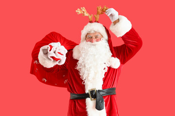 Santa Claus in deer horns with Christmas bag on red background
