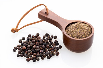 Ground black pepper in a measuring spoon with whole peppercorns on a white background