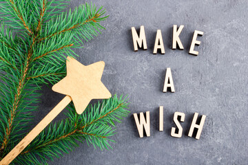 Text MAKE A WISH made from wooden letters. Christmas tree branch with magic wand with a star. Xmas and New Year's concept.