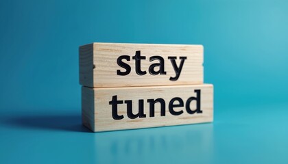 Conceptual shot presents two stacked wood blocks. Words Stay Tuned imprinted on wooden cubes. Object stands out against blue backdrop. Image evokes anticipation, invites viewer to look forward future