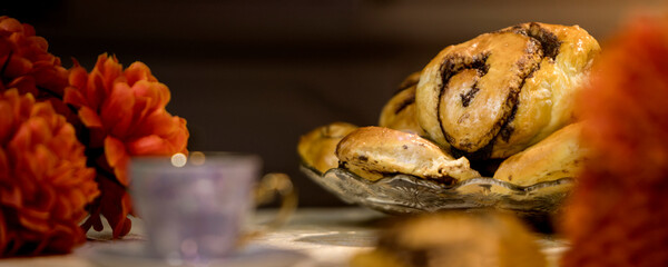A natural panoramic photo of delicious homemade baked goods. Rolled yeast rolls, chocolate-filled buns. Dessert with flowers and a marbled cup. Elegance, just like Mom's. Warm coffee tones.