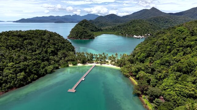 Experience the stunning beauty of Ko Ngam Beach in Koh Chang, Thailand. Lush greenery, clear turquoise waters, and a serene pier create a picturesque tropical paradise.