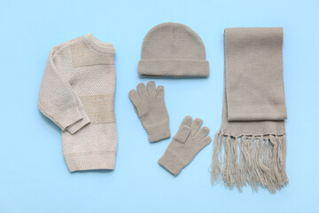 Stylish children's sweater, scarf, hat and gloves on blue background
