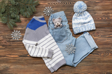 Stylish children's sweater, jeans, toy, hat, fir tree branch and decorative snowflakes on wooden...