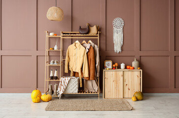 Chest of drawers, rack with clothes, accessories and pumpkins in interior of hallway