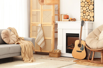 Interior of living room with sofa, armchair, closet, guitar, fireplace and autumn home decor near...