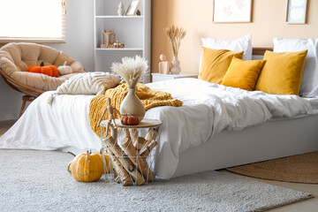 Interior of modern bedroom with comfortable bed, table, firewood and pumpkins