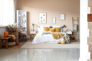 Interior of modern bedroom with comfortable bed, bench, shelving unit and pumpkins