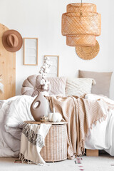 Comfortable bed, wicker table and vase with cotton flowers in interior of bedroom