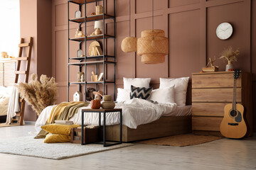 Interior of modern bedroom with comfortable bed, table, chest of drawers and guitar