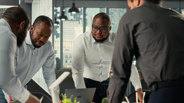Employees and coworkers discussing business intel and performance metrics in meeting. Multinational company work team reviews reports, forecasts and diagrams to align strategy. Camera B.